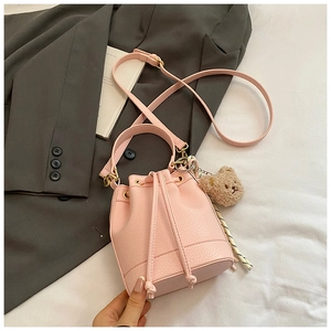 Detail of light pink drawstring bucket bag featuring brown teddy bear charm and striped rope