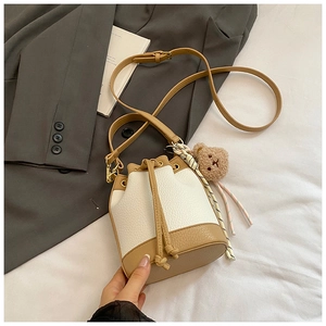Lifestyle shot of bicolor bucket bag with cute bear charm and scarf on white fabric