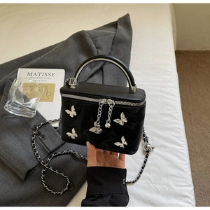 Close-up of black glossy handbag with silver metal butterflies and chain strap detail