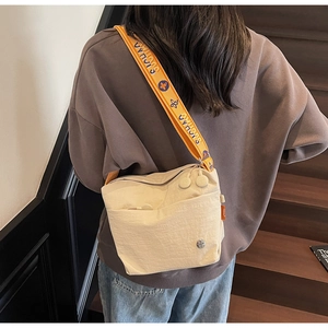Detail view of contrast orange woven strap on a beige canvas crossbody bag for women