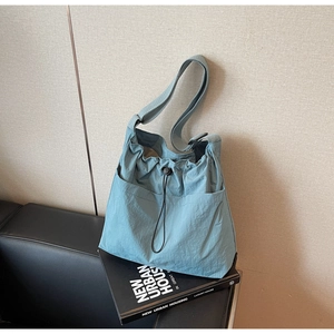 Close-up of a blue nylon drawstring bucket bag with adjustable strap on a leather sofa