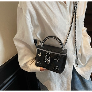 Detail of a black glossy vanity bag with metallic silver bow and chain strap