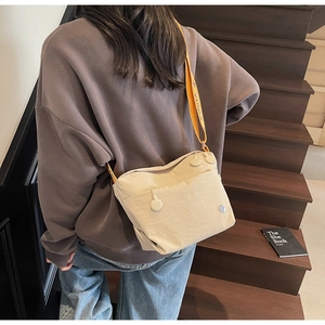 Detail view of beige crossbody bag with textured fabric and wide yellow logo shoulder strap