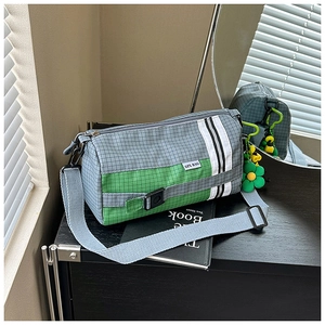 Détail du sac cylindrique en nylon à carreaux vert et gris avec un charm de marguerite
