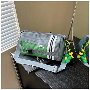 Détail du sac cylindre en nylon à carreaux gris-vert avec sangle et pendentif marguerite