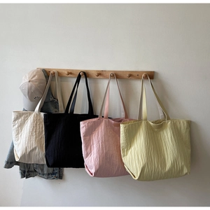 Detail of four colorful pleated tote bags in beige, black, pink, and yellow colors