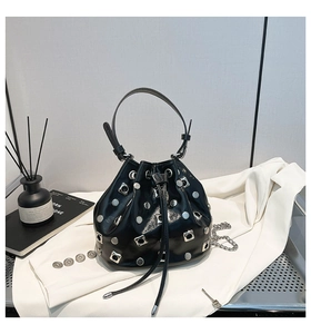 Close-up of black drawstring bucket bag with silver studs and metal chain strap details