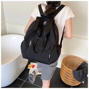 Detail of a black waterproof nylon backpack featuring a front flap pocket and side drawstring