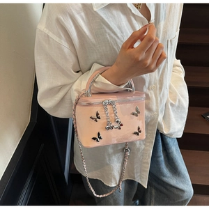 Detail of pink patent leather box bag featuring a metal bow accent and chain strap