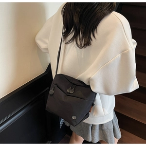 Detail of black nylon crossbody bag featuring front drawstring pocket and round logo