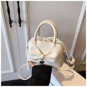 Détail du sac seau couleur crème avec grand nœud décoratif et pendentif cœur