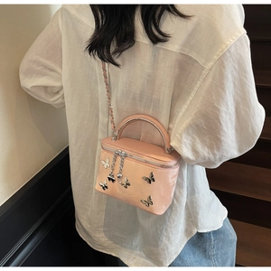 Detail of pink patent leather bag with silver butterfly charms and chain strap on shoulder