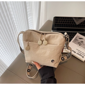 Close-up of wide patterned strap and zipper detail on beige canvas crossbody bag