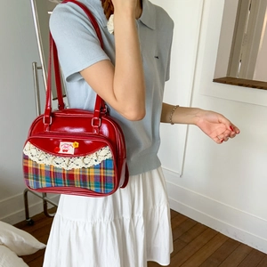 Detail of red patent leather tote bag with rainbow plaid trim and lace accents
