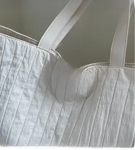 Close-up of beige tote bag with pleated texture and embossed leather brand logo tag