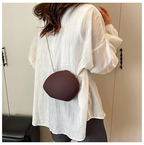 Détail du sac bandoulière bordeaux en forme de galet avec une chaîne dorée chic