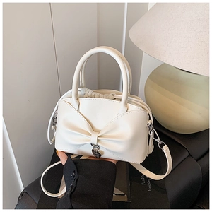 Détail du sac seau blanc crème avec un grand nœud et un pendentif coeur en métal poli