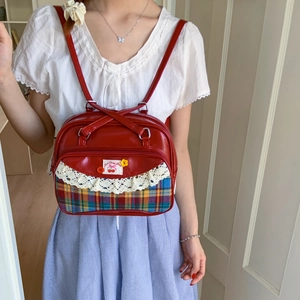 Detail of red leather tote bag with lace trim, cherry patch, and checkered fabric pattern