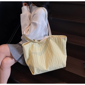 Detail of light yellow pleated tote bag with cream leather strap and embossed branding