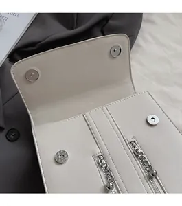 Détail du sac beige en similicuir grainé montrant les boucles magnétiques et poches zippées