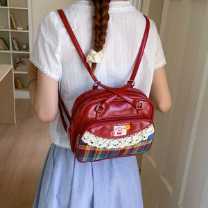 Detail of red cherry backpack with lace trim and plaid fabric on model back