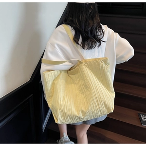 Detail of a bright yellow pleated tote bag showing fabric texture and embossed brand logo