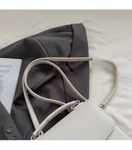 Gros plan du sac bandoulière en cuir crème montrant le grain de litchi et gravure BAG