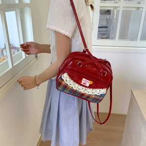 Detail of red patent leather tote with white lace trim and plaid pattern accents