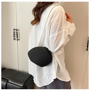 Détail d'un sac à bandoulière en acrylique noir en forme de galet avec chaîne dorée
