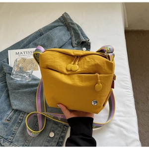 Detail of yellow nylon crossbody bag with patterned wide strap on artistic background