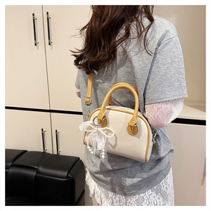Detail of beige litchi grain Boston bag with yellow handles and lace bow charm