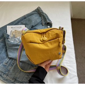 Detail of yellow canvas crossbody bag featuring a trendy purple and yellow wide strap