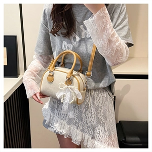 Detail view of lychee texture cream Boston bag with ginger trim and lace bow charm