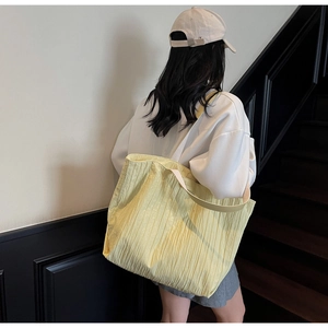 Close-up of yellow pleated fabric tote bag worn by model on a minimalist staircase