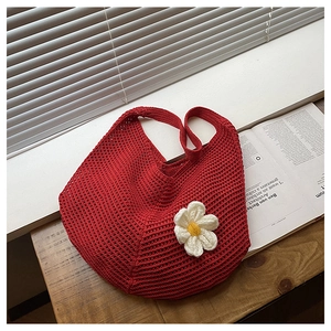 Gros plan d'un sac hobo rouge tressé avec fleur 3D blanche sur un banc en bois