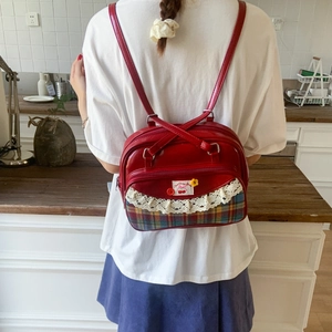 Detail of red patent leather backpack with lace trim and vintage plaid canvas texture