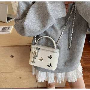 White square crossbody bag with silver butterfly charm and metal handle worn by model