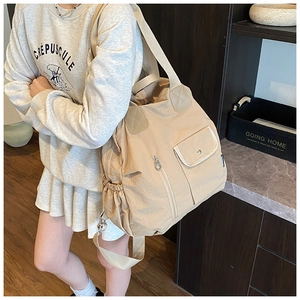 Detail of light beige nylon tote bag with functional pockets and drawstring on model