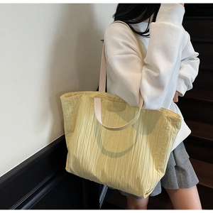 Close-up of bright yellow tote bag featuring pleated texture and rectangular brand logo