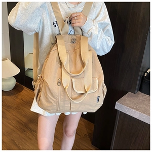 Detail view of beige multi-pocket backpack with wide straps and smooth metal zippers