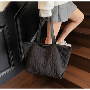Detail showing vertical pleated texture and leather logo patch of black tote bag