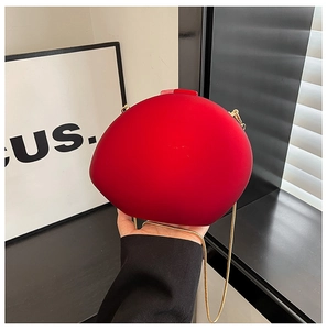 Gros plan d'un sac de soirée rond rouge avec chaîne dorée et texture veloutée mate