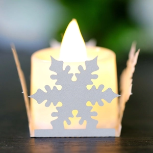 Detail of warm LED candle with white laser-cut snowflake paper sleeve for Christmas
