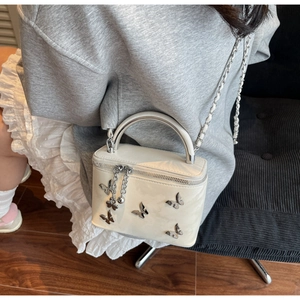 Detail of cream white box bag featuring metallic butterfly accents and silver chain strap