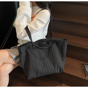 Close-up of the pleated fabric texture and leather logo detail on a black tote bag