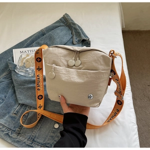 Close-up of beige nylon crossbody bag with orange jacquard strap and zip pocket