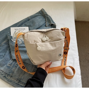 Detail of beige nylon crossbody bag featuring orange woven strap and metal logo accent