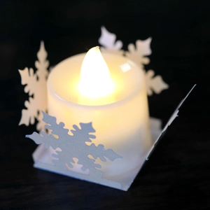 Macro view of LED candle with warm yellow light and cutout snowflake paper holder