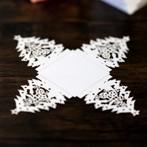 Macro detail of laser-cut Christmas tree patterns on white pearlescent paper gift box