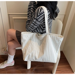 Detail of white tote bag with pleated texture and embossed brand logo in casual setting